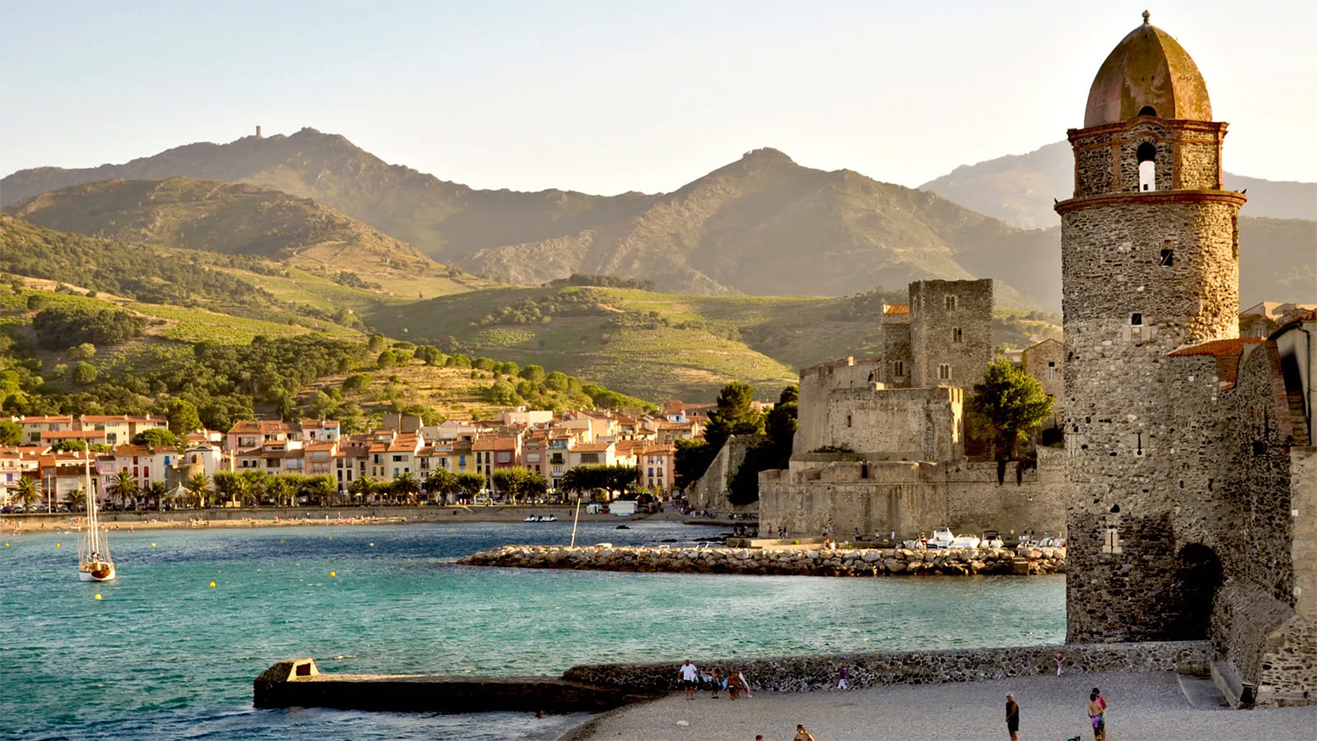 Vue de la plage de Collioure avec le château royal, le clocher Notre-Dame-des-Anges et les montagnes des Albères en arrière-plan.