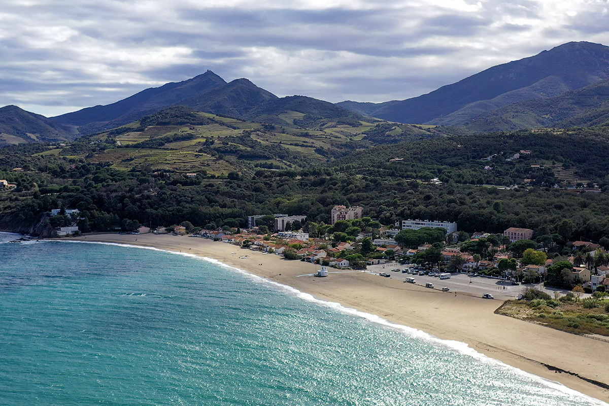 Vue aérienne de la plage du Racou à Argelès-sur-Mer entre la Méditerranée, les Albères et les premières maisons du village.