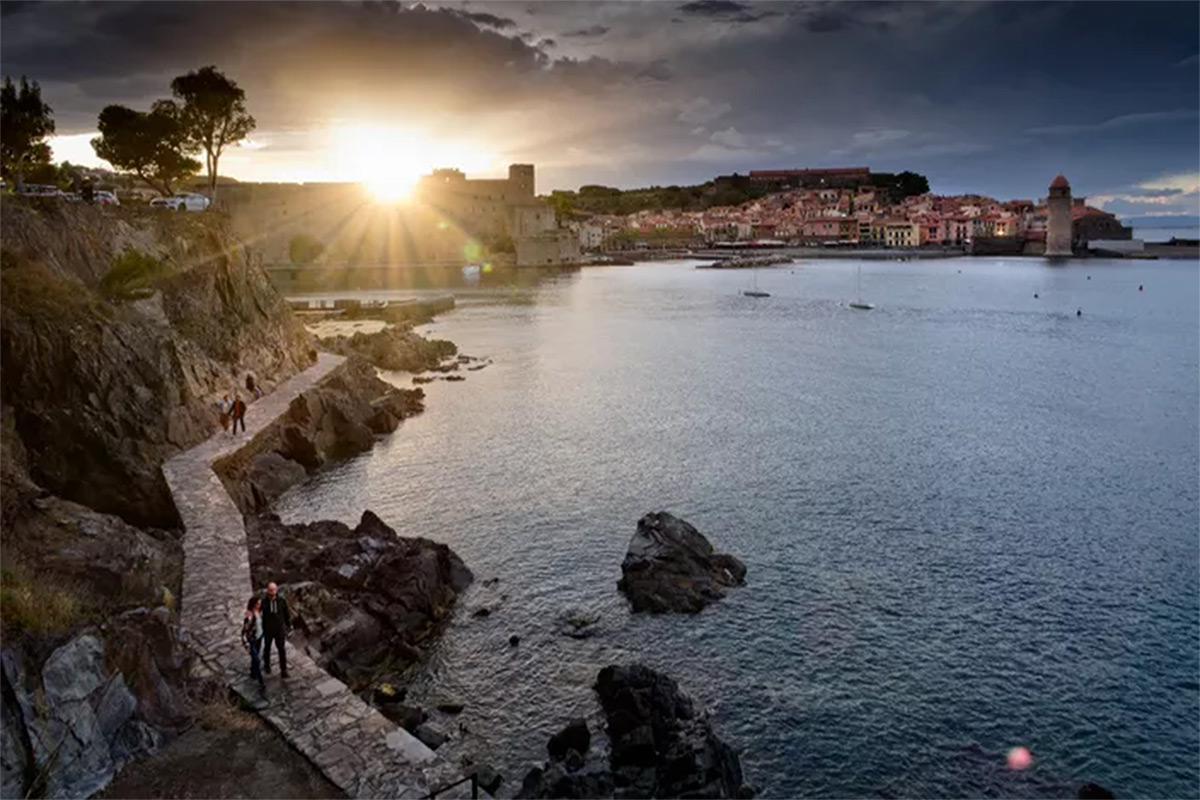 Le sentier du littoral reliant la plage du Racou à Collioure avec une vue sur la baie et le village au coucher du soleil.
