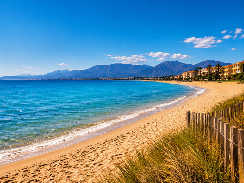Vue panoramique de la plage de Canet-en-Roussillon avec la mer Méditerranée, son sable fin et les montagnes des Pyrénées en arrière-plan.